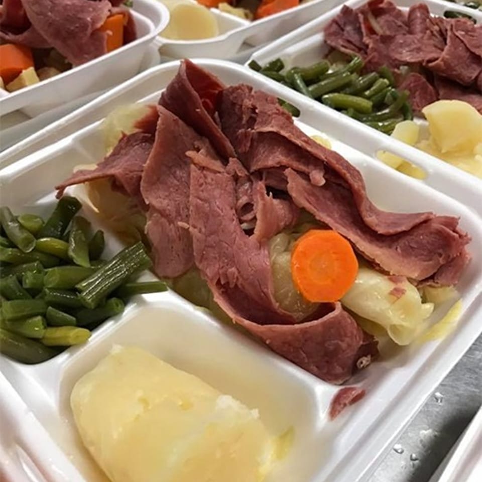 Compartmented trays hold sliced corned beef with cabbage, carrots, green beans, potatoes, and gravy.