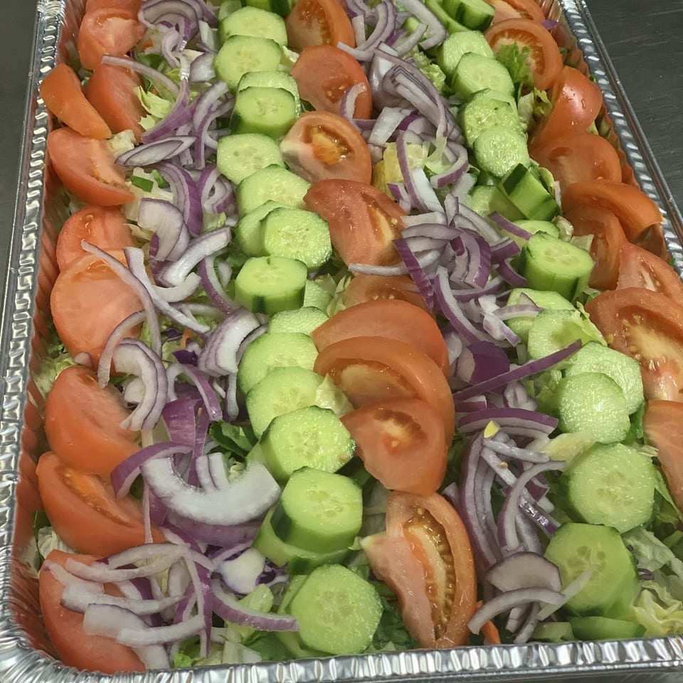 Fresh chopped salad with lettuce, sliced tomatoes, cucumbers, and red onions in a large foil catering tray.